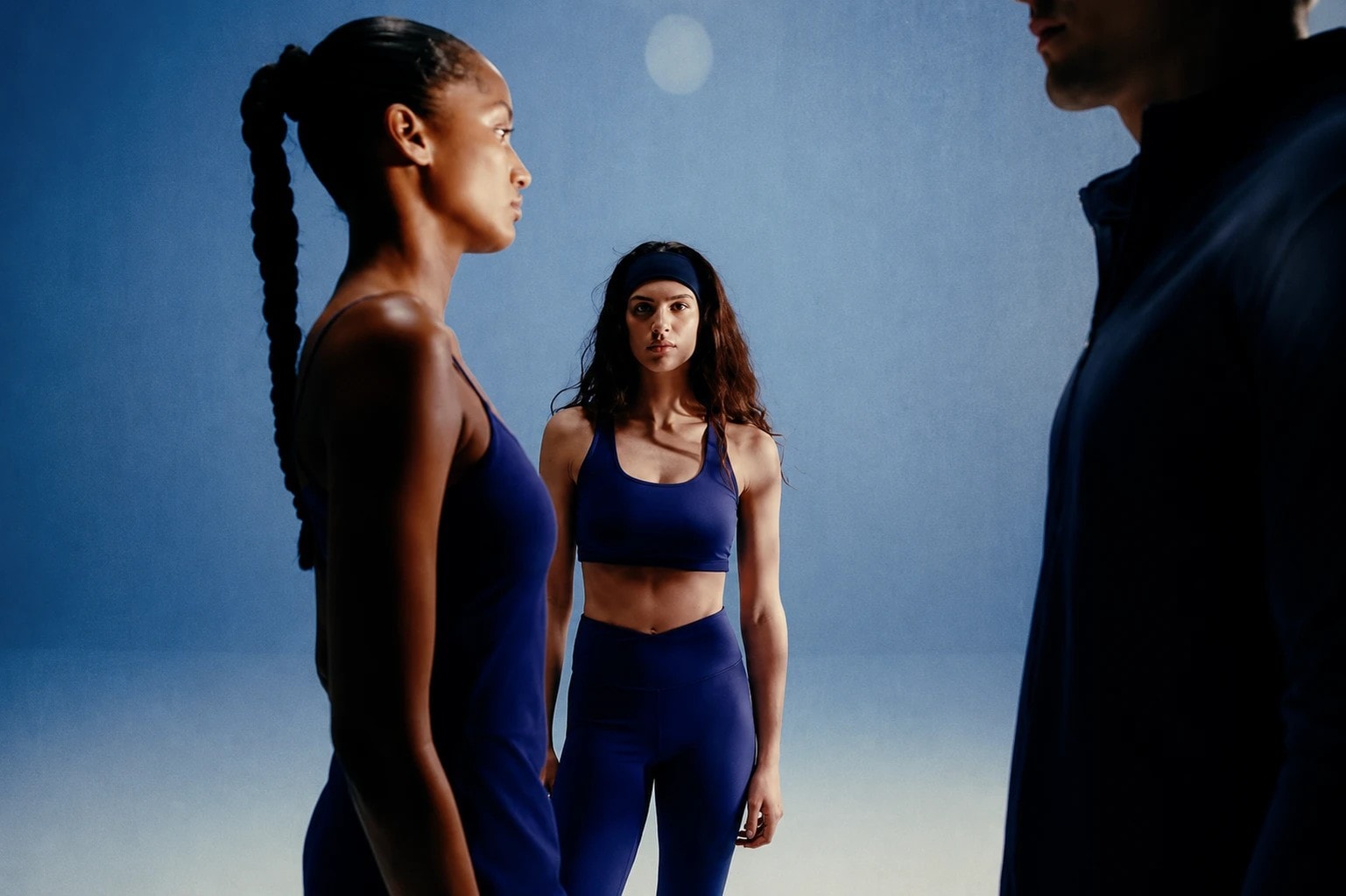 Three athletes in dark training kit standing together, moodily lit in blue